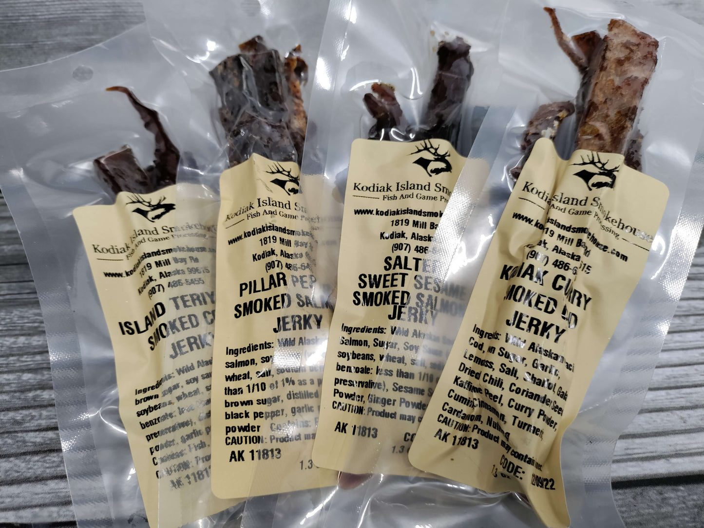 Four vacuum-sealed bags of assorted wild Alaskan smoked fish jerky sampler flavors.