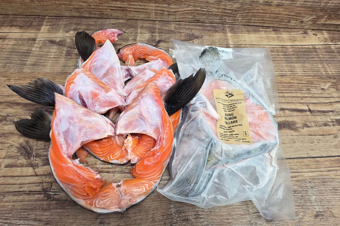 Vacuum-sealed wild Alaskan King Salmon collars beside fresh collars on a rustic wooden surface, showing packaging and product size.