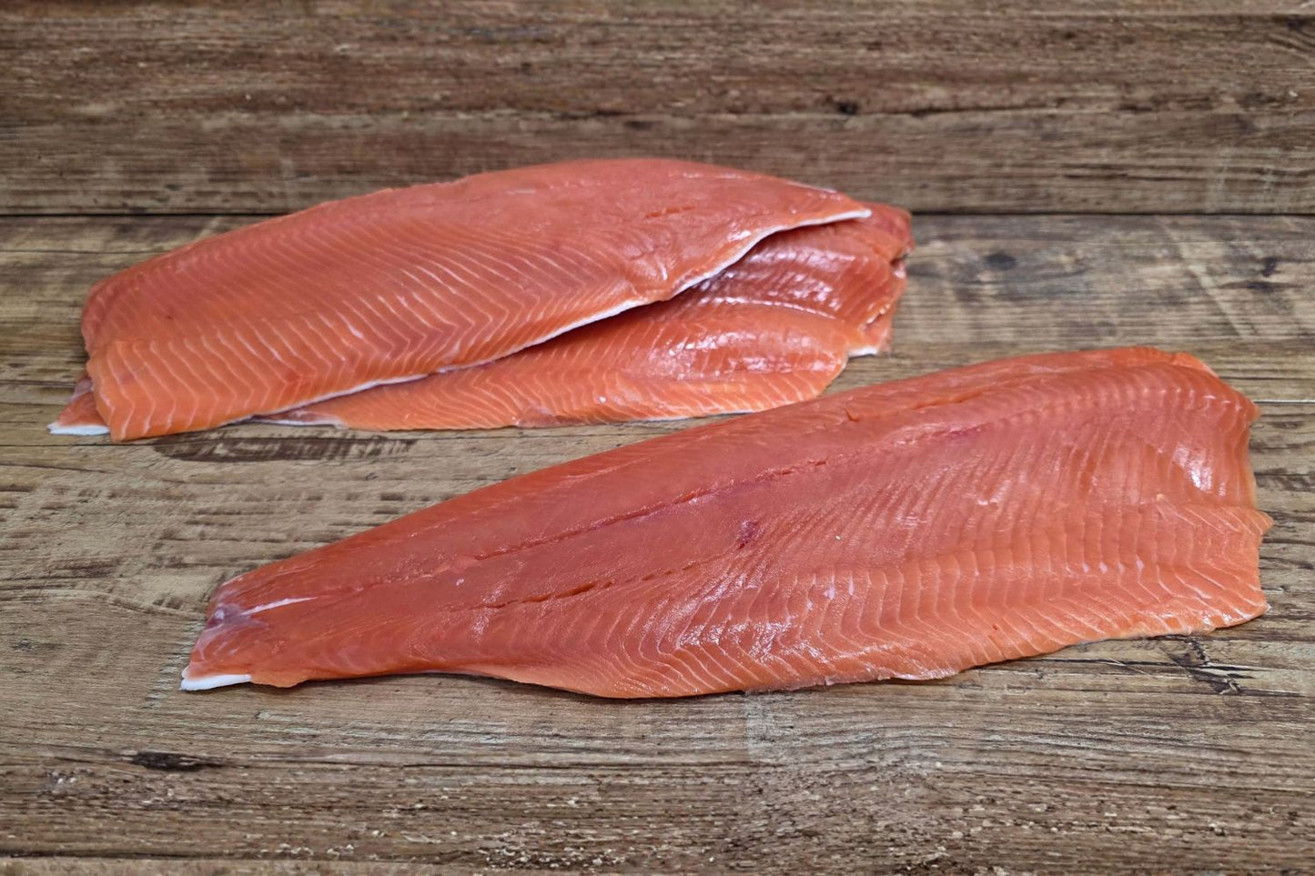 Raw Wild Alaskan coho salmon fillets laid out on a rustic wood surface, showing their bright red-orange color and clean trim.
