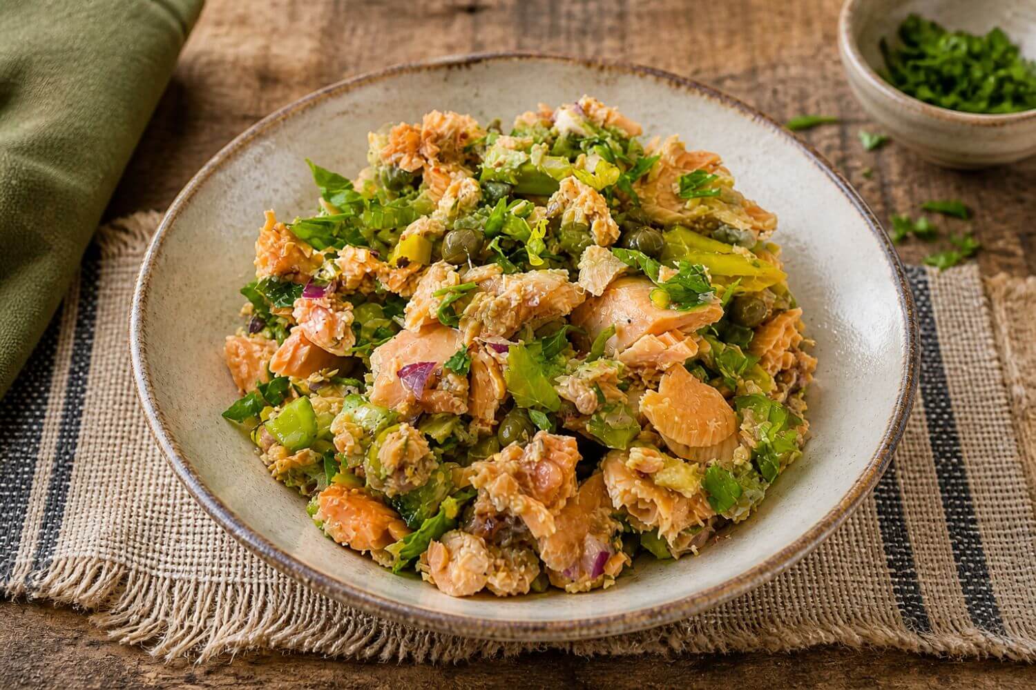 Salmon salad with celery, capers, and red onion in a rustic ceramic bowl on a wooden table in natural light