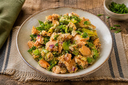 Salmon salad with celery, capers, and red onion in a rustic ceramic bowl on a wooden table in natural light