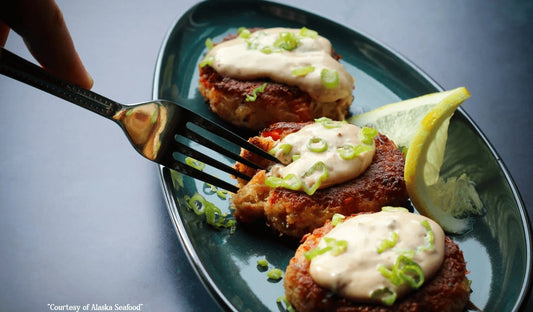 A plate of golden-brown Alaska crab cakes, crisp on the outside and tender inside, served with lemon wedges and dipping sauce.