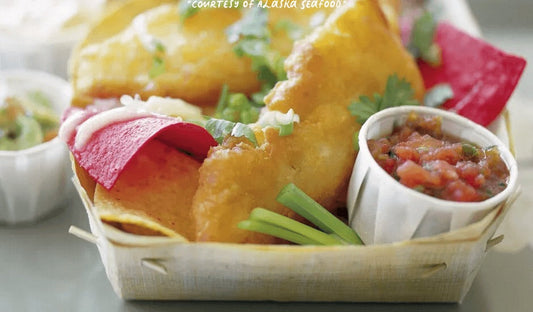 Golden-fried Alaska halibut pieces layered over tortilla chips, topped with roasted poblano salsa and drizzled with chipotle tartar sauce, served on a rustic platter.