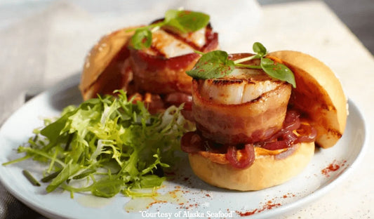 Mini sliders made with bacon-wrapped Alaska Weathervane Scallops, layered with pimenton-spiced mayonnaise, balsamic caramelized red onions, and lettuce on toasted mini buns, arranged on a rustic serving board.