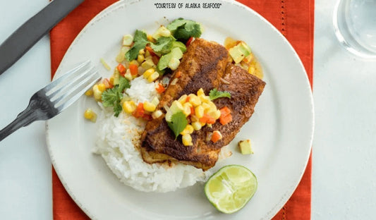 Pan-seared Alaska rockfish fillets coated in Cajun spices, topped with avocado-corn salsa, served over sticky rice on a rustic plate.