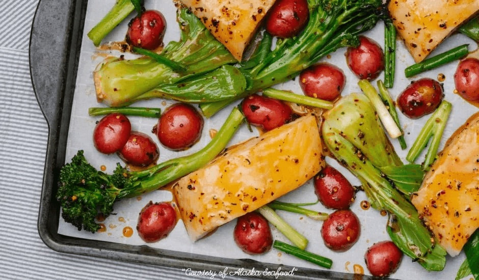 Sheet pan with roasted Alaska sablefish (black cod) glazed in chili crisp sauce, surrounded by colorful vegetables like bell peppers and onions, served hot and caramelized.