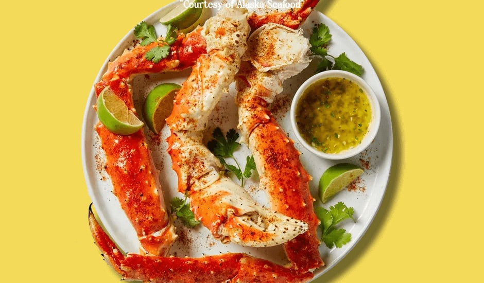 Plated Alaska King Crab legs served with jalapeño-cilantro butter and lime wedges, served on a rustic dish.