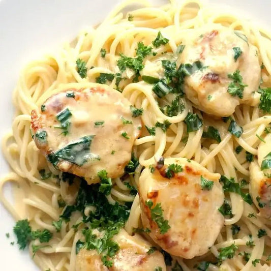 Pan-seared scallops in a creamy garlic sauce served over linguine, garnished with parsley on a white plate.