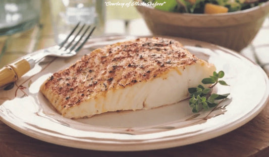 Alaska halibut fillet coated in a spicy dry rub, grilled to golden perfection and served with a fresh garnish on a ceramic plate.