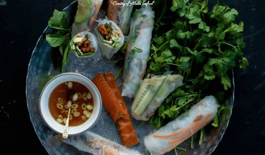 Fresh rolls filled with Alaska smoked salmon, crisp vegetables, basil on a plate with dipping sauce and fresh herbs.