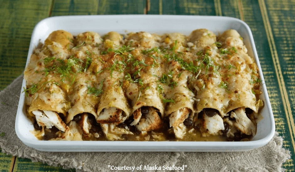 A pan of halibut enchiladas topped with salsa verde, melted cheese, and cilantro, featuring flaky wild Alaska halibut and golden edges.