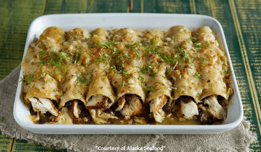 A pan of halibut enchiladas topped with salsa verde, melted cheese, and cilantro, featuring flaky wild Alaska halibut and golden edges.