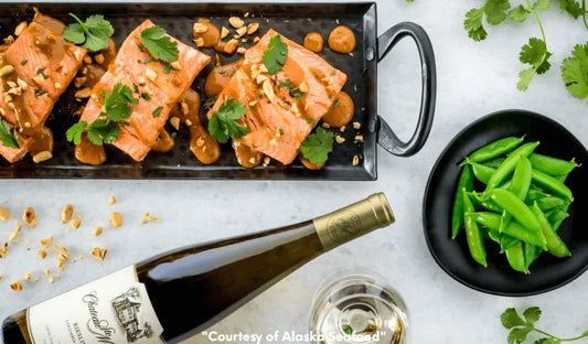 Wild Alaska salmon fillets cooked in a peanut sauce with soy, lime, ginger, and Sriracha, garnished with chopped peanuts and cilantro, served in a shallow bowl.