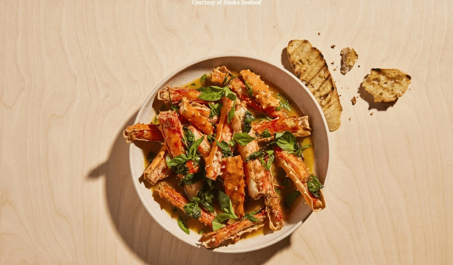 Alaska king crab legs served mariner-style with a glossy sauce of sake, butter, soy, and ginger, topped with scallions and Thai basil.