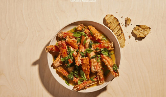 Alaska king crab legs served mariner-style with a glossy sauce of sake, butter, soy, and ginger, topped with scallions and Thai basil.