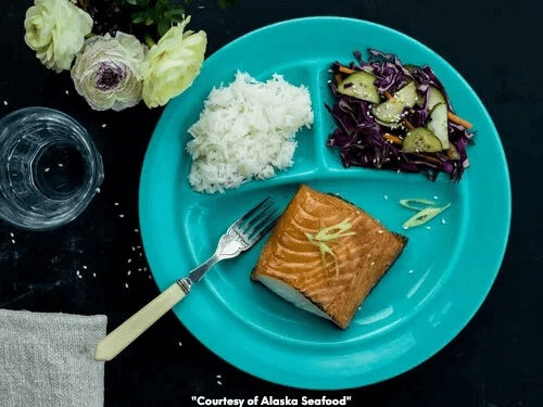Miso-glazed Alaska black cod served with steamed white rice and Asian cucumber slaw on a turquoise plate.