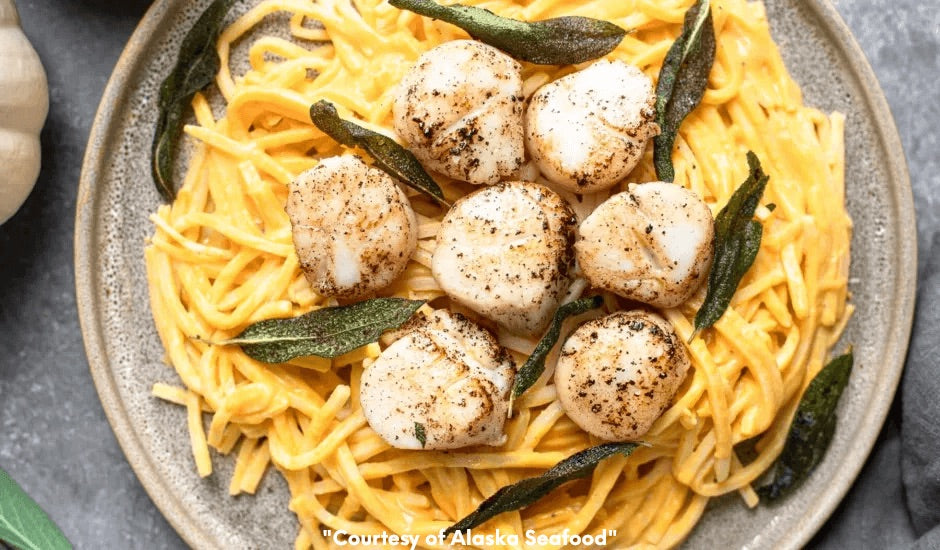 Pan-seared Alaska scallops served atop pumpkin Alfredo sauce with hearts of palm linguine, garnished with crispy sage leaves on a rustic ceramic plate.