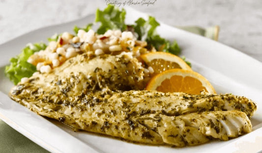 Pan-seared Alaska rockfish fillets drizzled with bright green chermoula sauce, garnished with fresh herbs and lemon slices, served on a white plate.