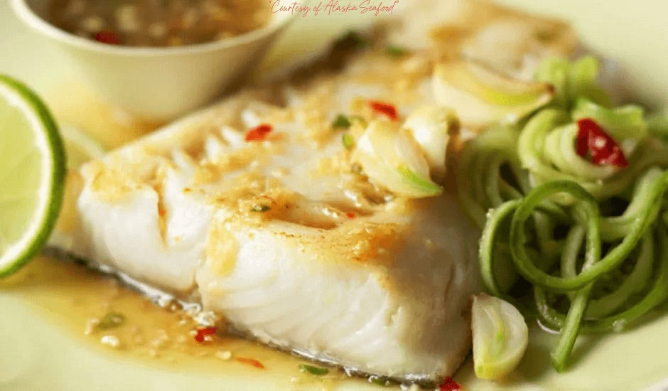 Alaska sablefish fillet pan-seared to golden perfection, topped with ginger-lime sauce and served over spiralized cucumber noodles on a rustic plate.