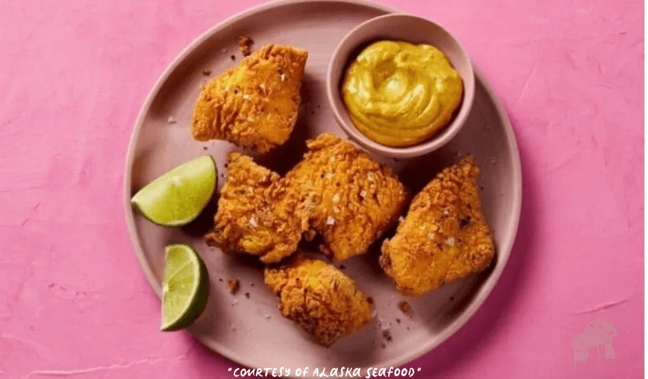 Golden-fried Alaska sablefish bites coated in curry-seasoned batter, served with a side of creamy masala aioli and lime wedges on a rustic plate.