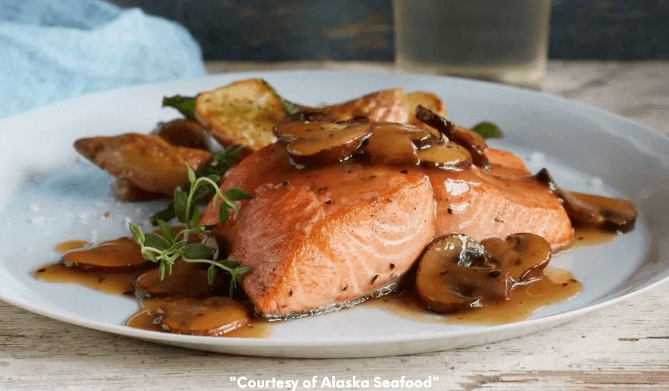Seared Alaska salmon fillets simmered in Marsala wine with mushrooms and thyme, plated with sauce and garnished with a fresh thyme sprig on a ceramic dish.