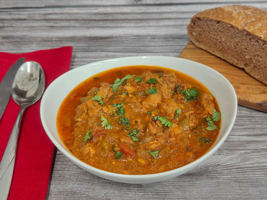 A bowl of Salmon Moqueca-Inspired Stew featuring wild Alaska salmon in a coconut milk broth with tomatoes, peppers, garlic, and cilantro, served hot.