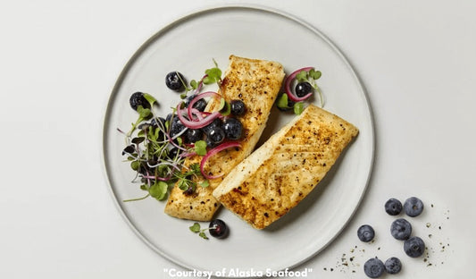 Golden-seared Alaska halibut fillet topped with pickled blueberries, plated with microgreens and seasonal accents on a ceramic plate.