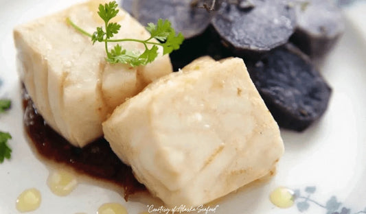 Alaska halibut fillet steamed in whiskey, served with a light glaze and rustic sides on a warm-toned plate.