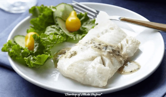 Alaska white fish fillet poached in white wine and served with lemon butter herb sauce, garnished with fresh herbs and plated with a light vegetable side.