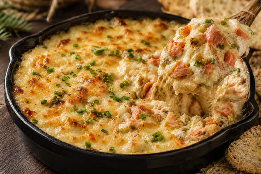 Hot smoked salmon caramelized onion dip served in a black skillet with crackers