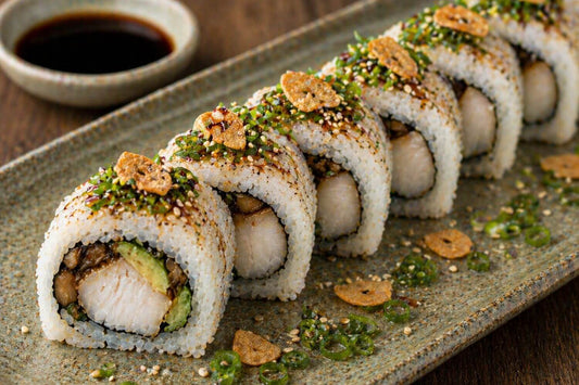 Umami black cod sushi roll with sautéed mushrooms, avocado, crispy garlic, sesame seeds, and a light soy drizzle on a ceramic plate
