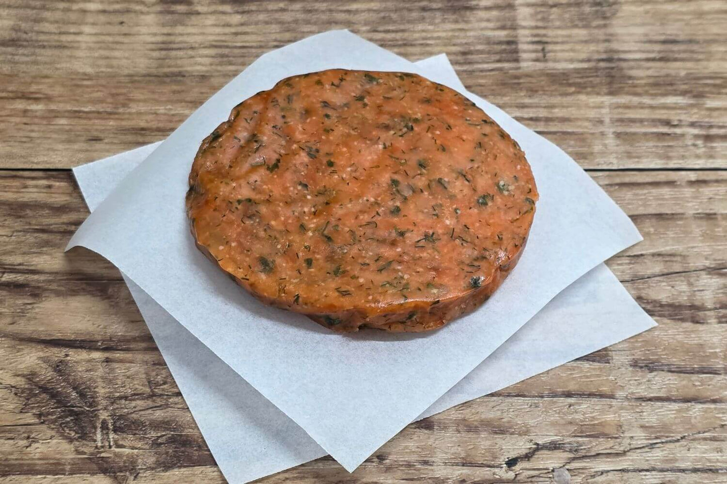 Grain-free Herbed Wild Alaskan salmon burger patty on parchment over rustic wood.