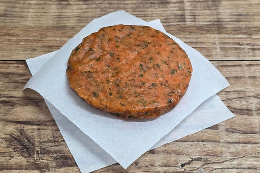 Grain-free Herbed Wild Alaskan salmon burger patty on parchment over rustic wood.
