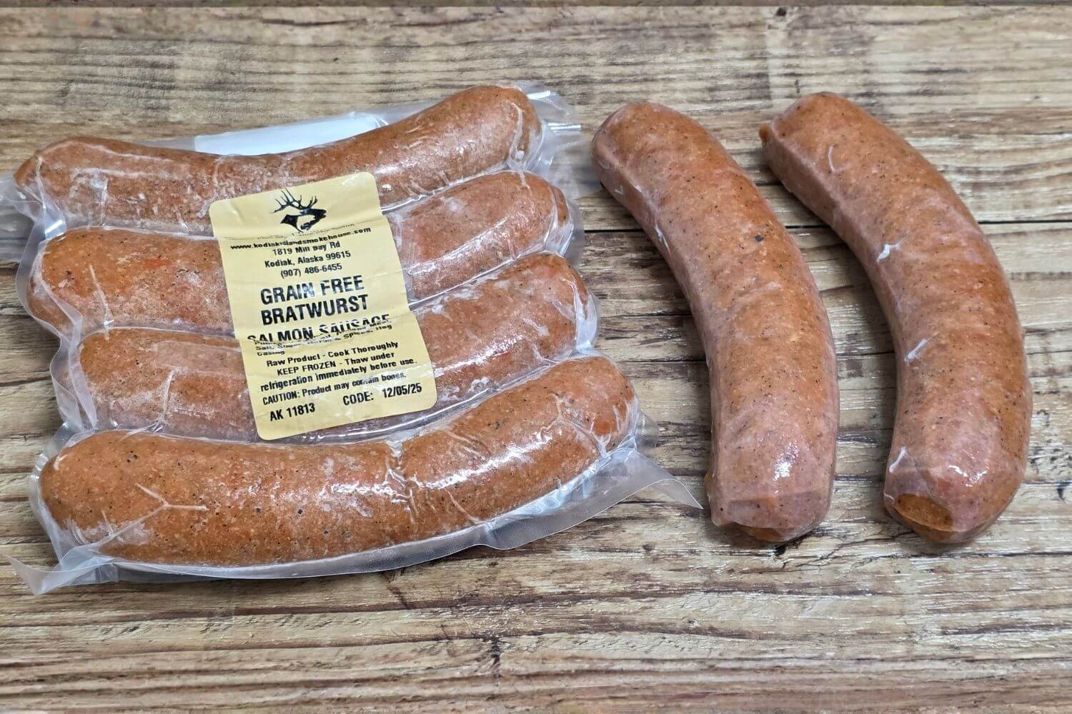 Wild Alaskan grain-free salmon bratwurst on rustic wood background, shown both vacuum-sealed and loose for a clear view of size and texture.