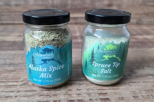 Adventure Harvest Alaska Spice Mix and Spruce Tip Salt seasoning jars displayed on wooden background.