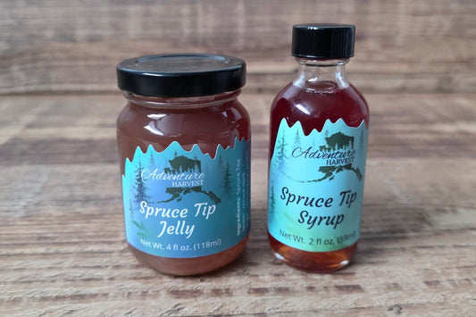 Wild Alaskan spruce tip jelly and spruce tip syrup from Adventure Harvest displayed in glass containers on a rustic wood surface.