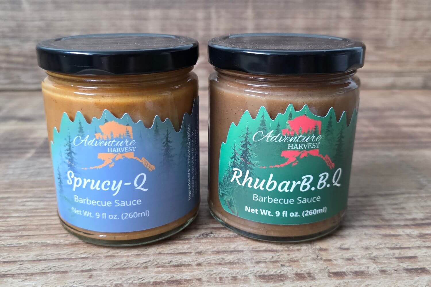 Adventure Harvest Sprucy-Q and RhubarB.B.Q. barbecue sauce jars displayed on a rustic wood background.