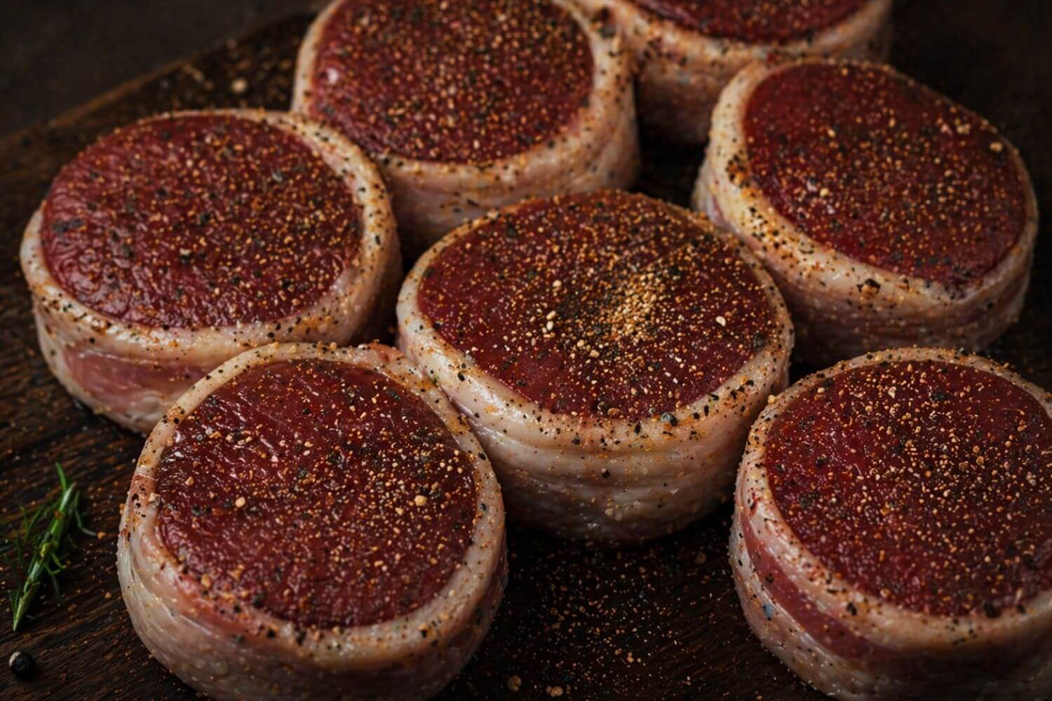 Bacon wrapped wild game backstrap steaks seasoned and ready for cooking on a wooden surface