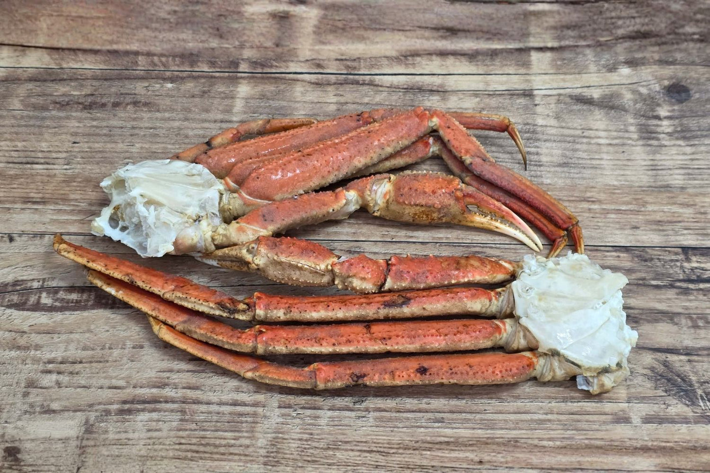 Wild Alaskan Bairdi crab cluster with intact legs and claws, fully cooked and displayed on rustic wood.