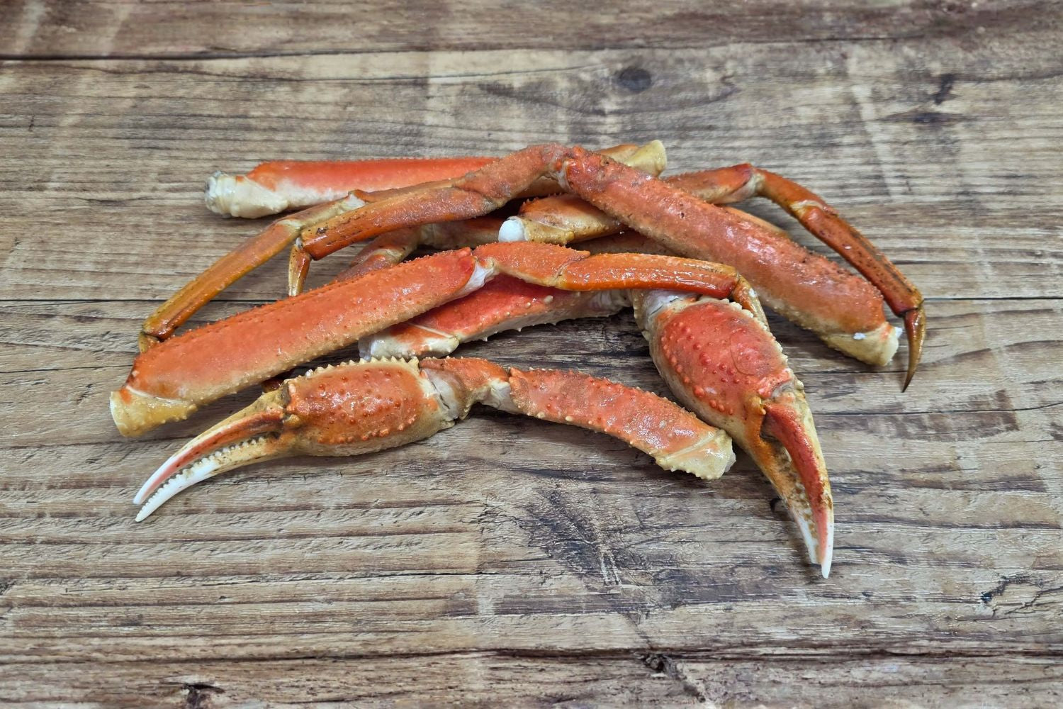 Cooked Wild Alaskan Bairdi (Tanner) crab legs and claws displayed on a rustic wood surface.
