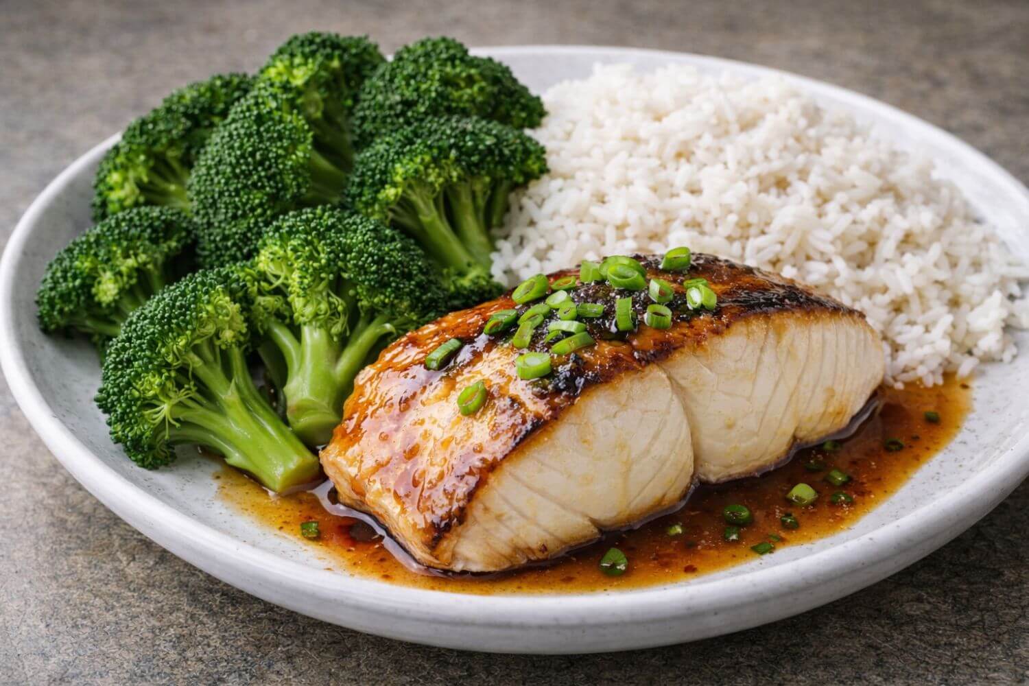 Plated dish with glazed black cod, broccoli, and rice on a gray surface