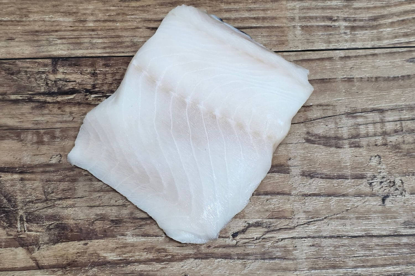 Raw Wild Alaskan black cod fillet on a rustic wood surface.