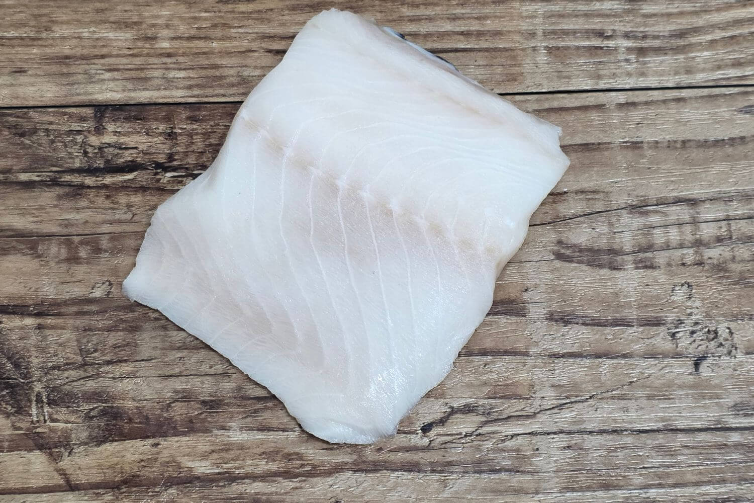 Raw Wild Alaskan black cod fillet on a rustic wood surface.