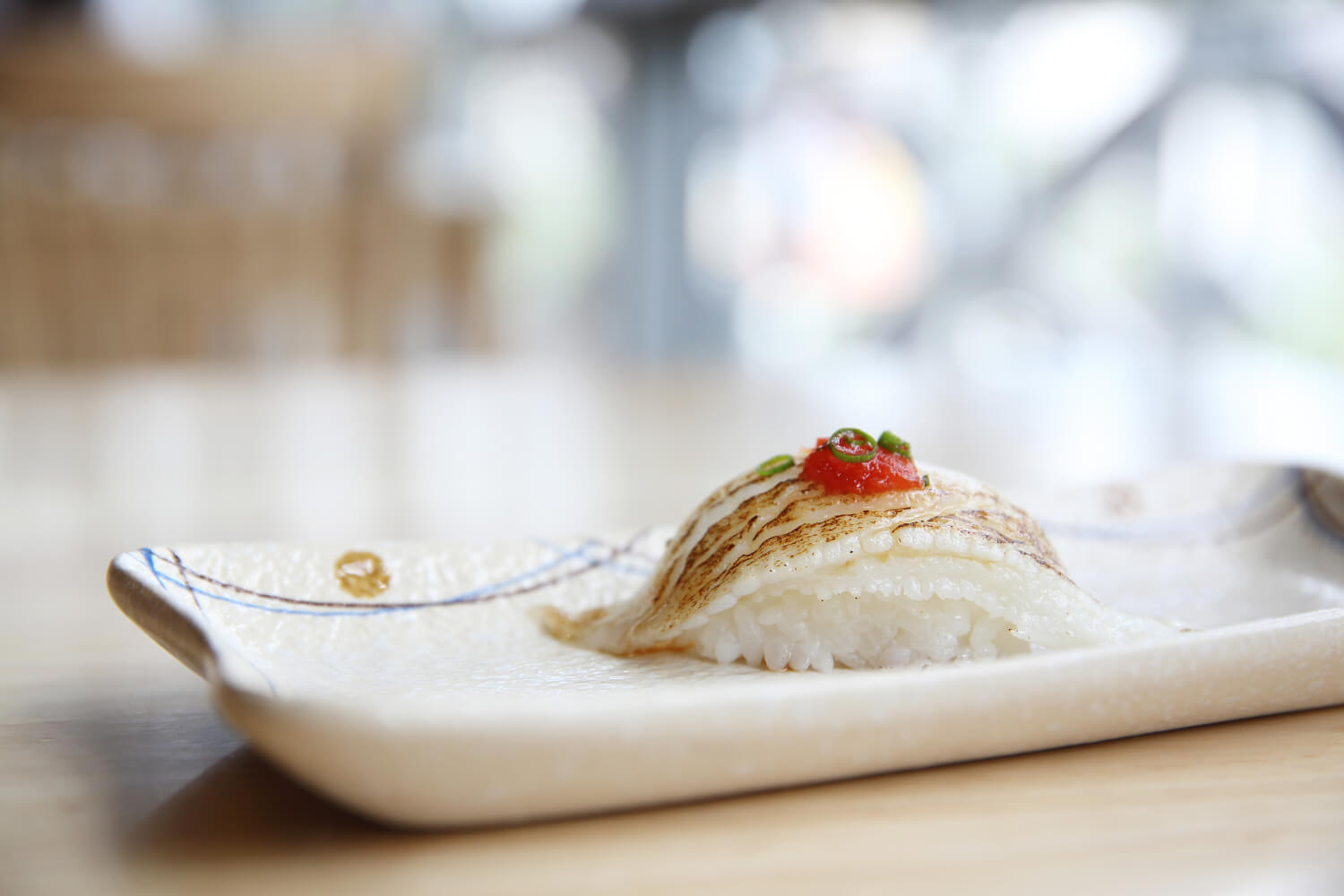 Aburi black cod nigiri, lightly seared, served on a rustic white plate.