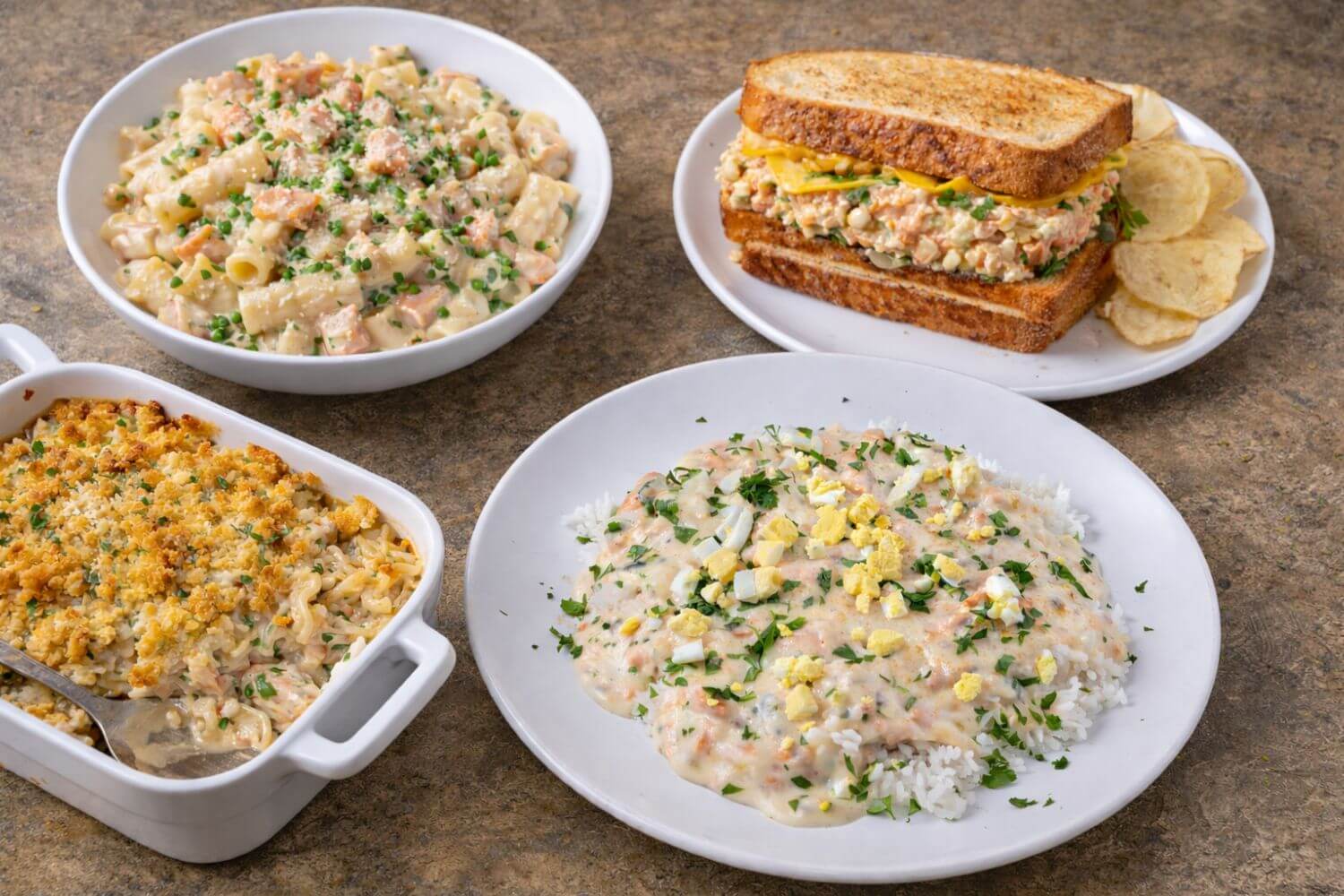 Assorted dishes including a casserole, macaroni salad, sandwich, and rice with cream sauce on a brown surface.