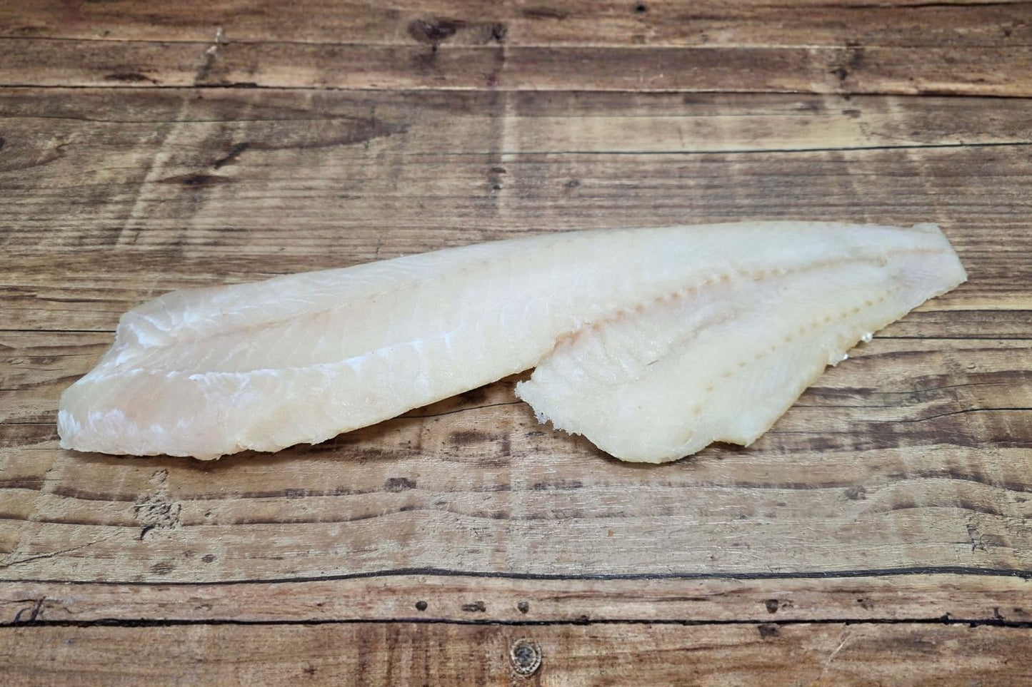 Wild Alaskan Pacific cod fillet on a rustic wood table, highlighting the mild white flesh typical of Kodiak-caught cod.