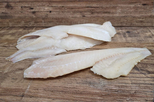 Raw Wild Alaskan cod fillets arranged on a rustic wood surface, showing their mild white flesh and clean texture.