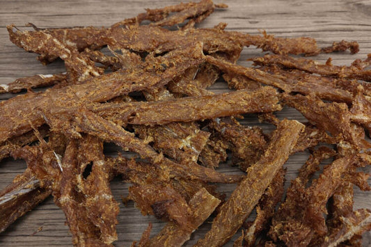 Smoked curry-seasoned wild cod jerky pieces on a wooden board.