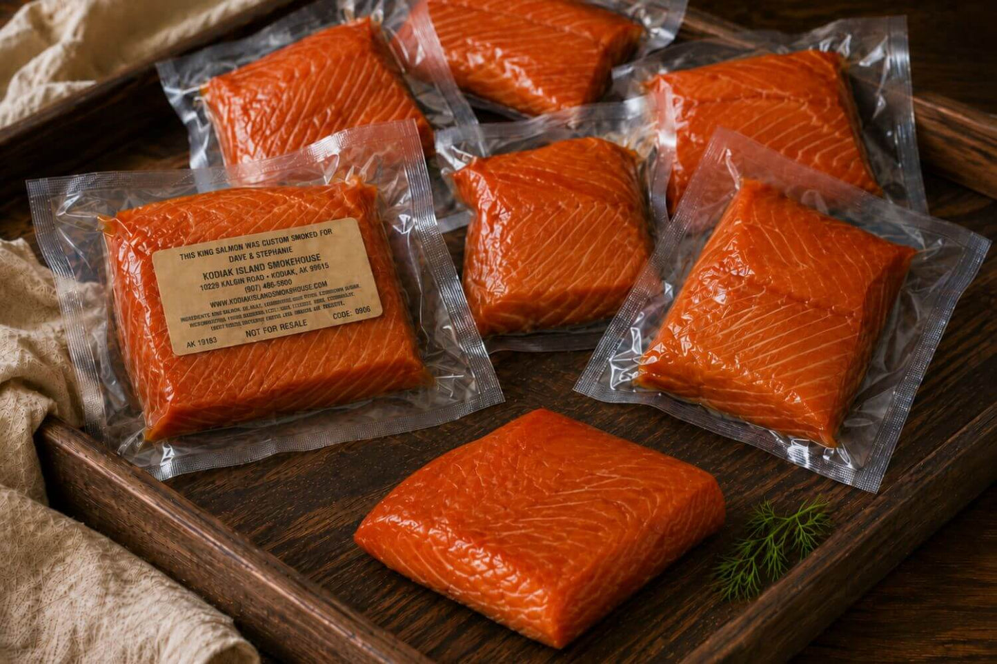 Personalized custom-smoked king salmon gift pack with vacuum-sealed portions and one unpackaged smoked king salmon piece arranged in a shallow wooden tray.