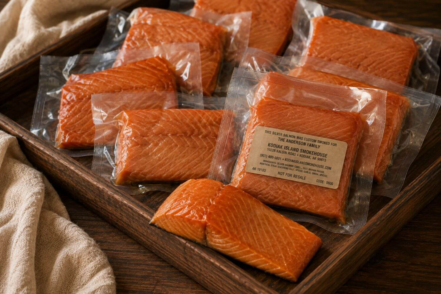 Personalized custom-smoked silver salmon gift pack with vacuum-sealed coho salmon portions and one unpackaged smoked salmon piece arranged in a shallow wooden tray.
